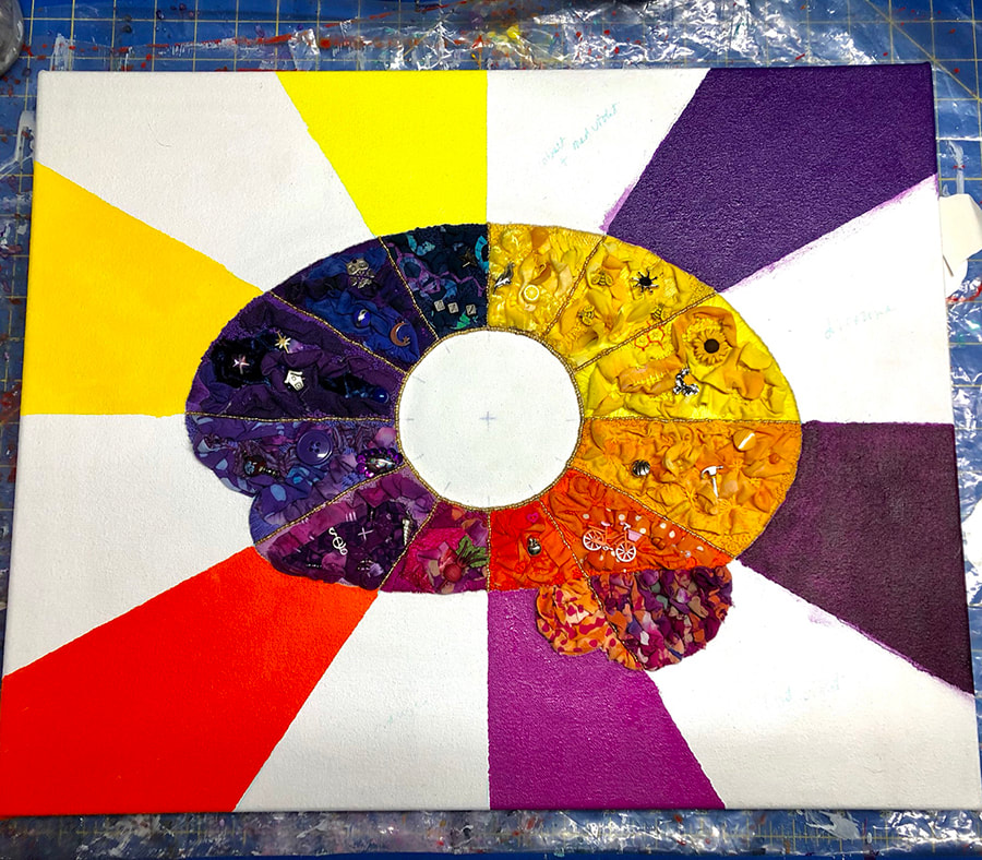 The finished fiber art bain with painted rays of purple, pink, red and yellow alternating with white coming out from it. In the middle of the brain is a plain white circle.